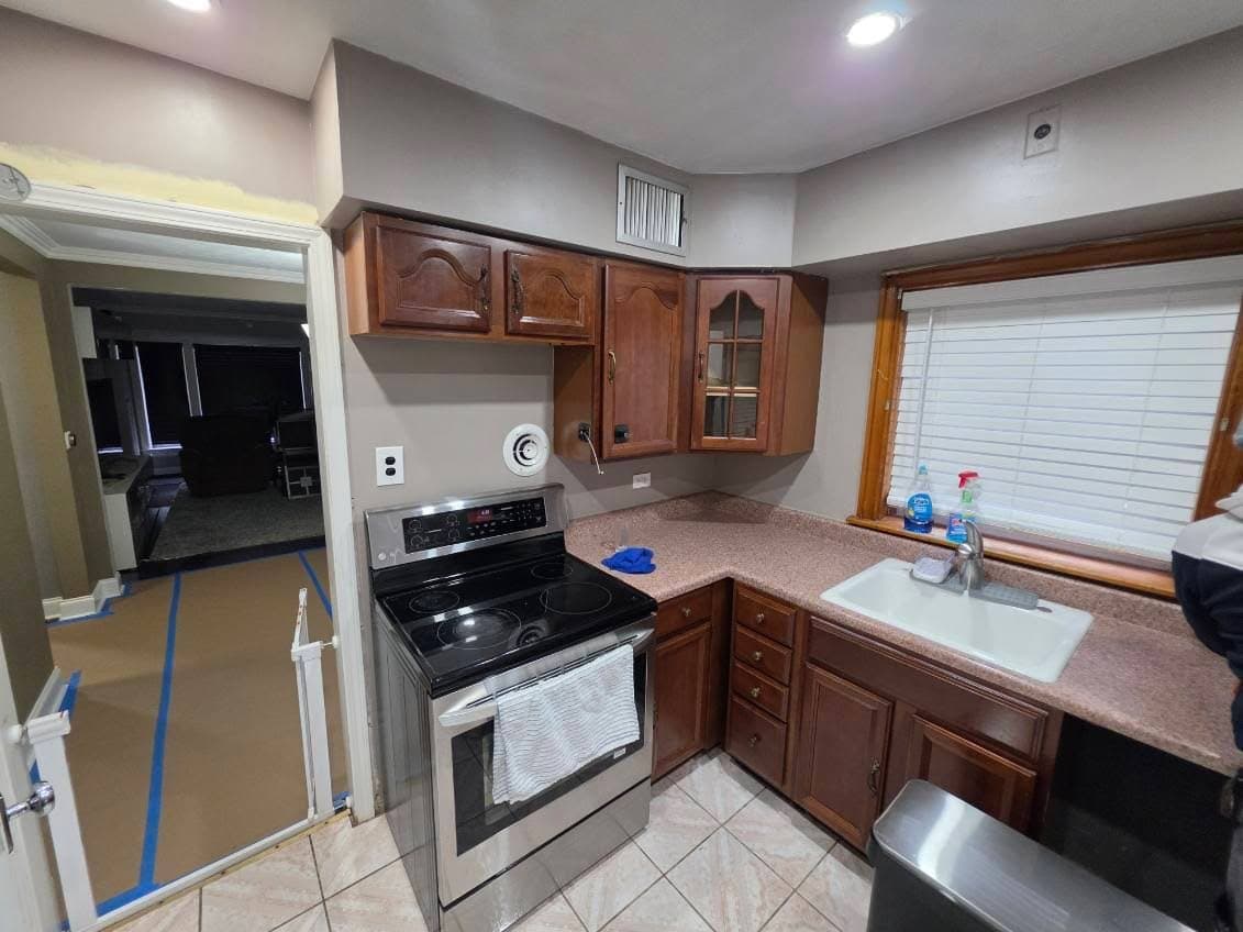 Existing kitchen before demolition, with dated oak cabinets, a laminate counter, a white drop-in sink and floor protection taped down in the next room