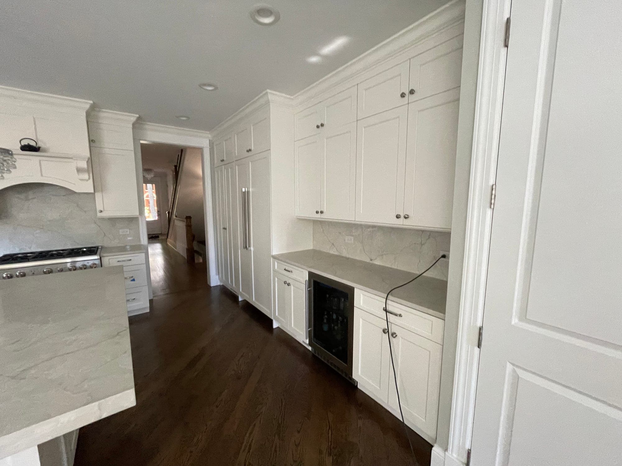 White Shaker cabinet wall with a paneled refrigerator, a beverage refrigerator and a veined counter and backsplash