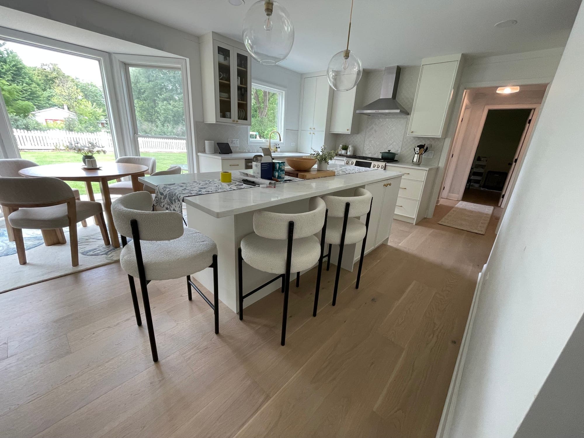 White kitchen island with a light veined top and three upholstered stools beside a round breakfast table