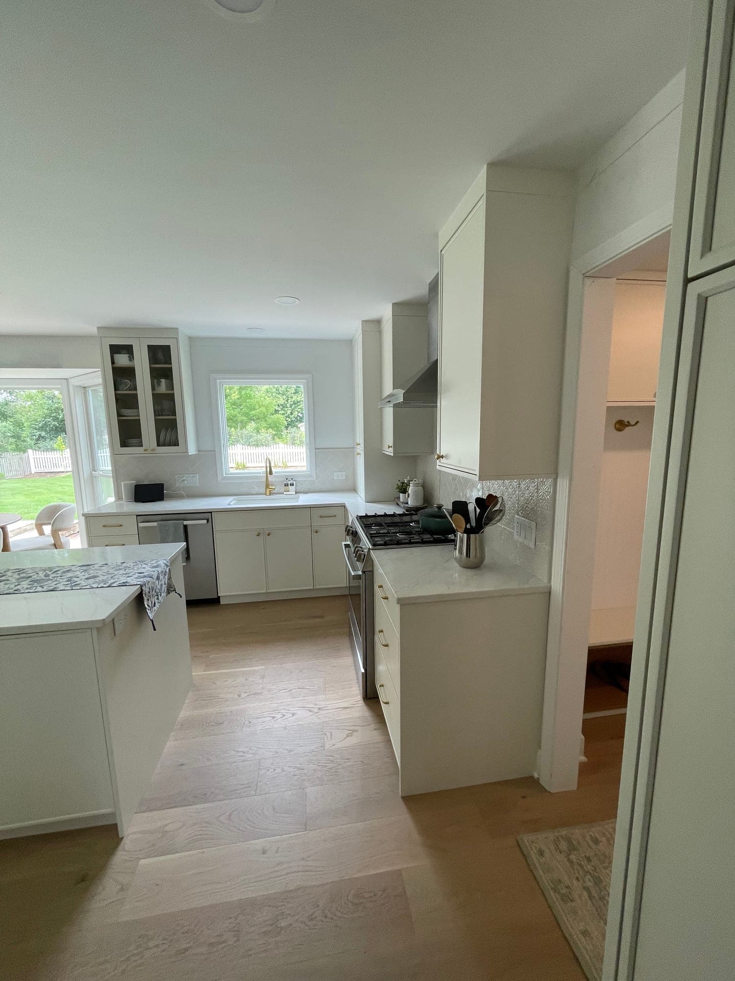 White flat panel kitchen with a stainless range and chimney hood, white tile and a window over the sink