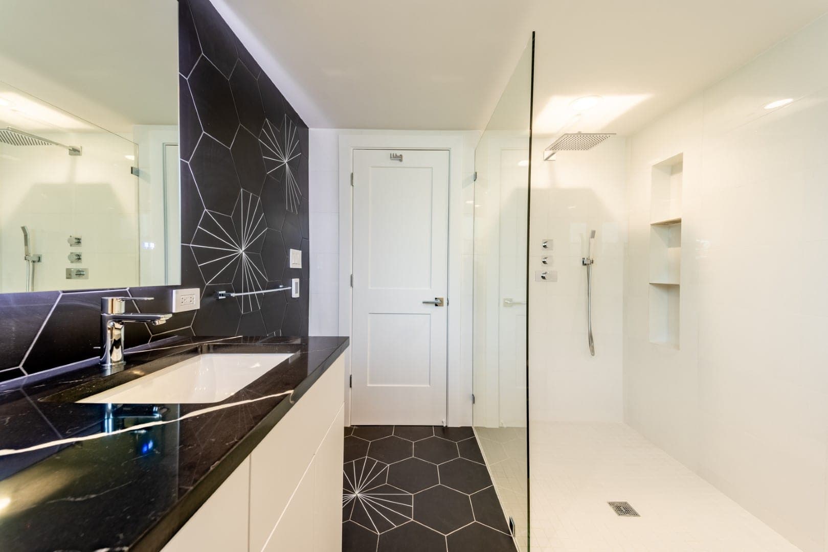 Bathroom with black hexagon tile on the wall and floor, a black veined vanity top and a glass walk-in shower
