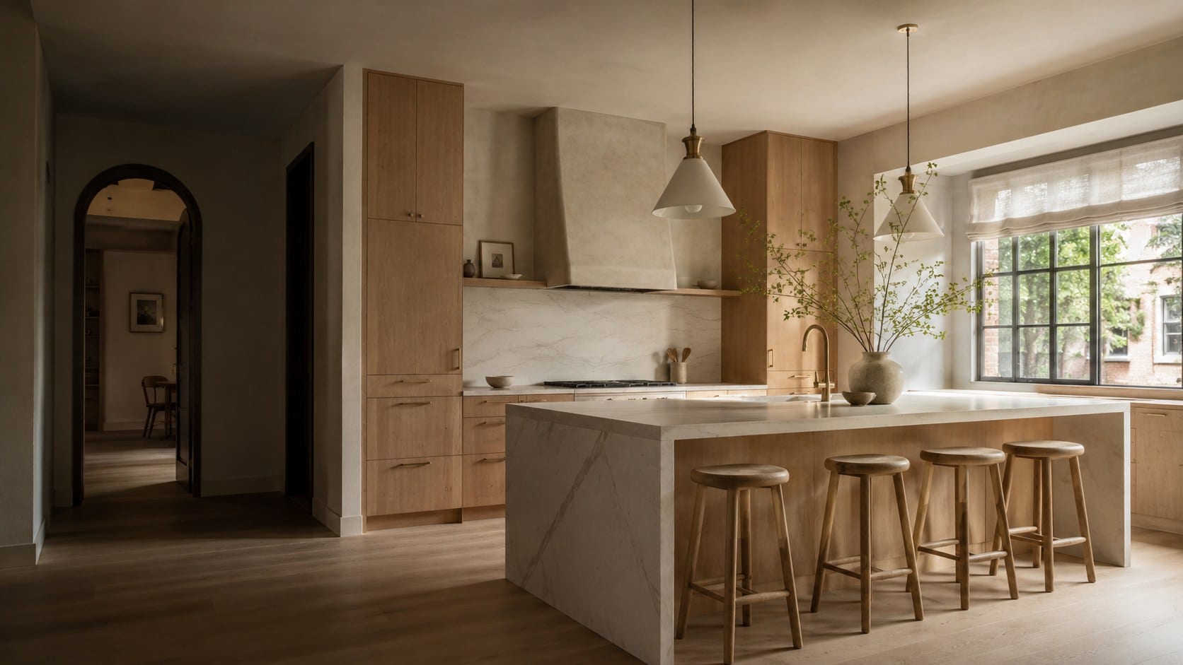 Wide kitchen with white oak cabinetry, a plaster range hood, a waterfall marble island with four oak stools and a large steel window