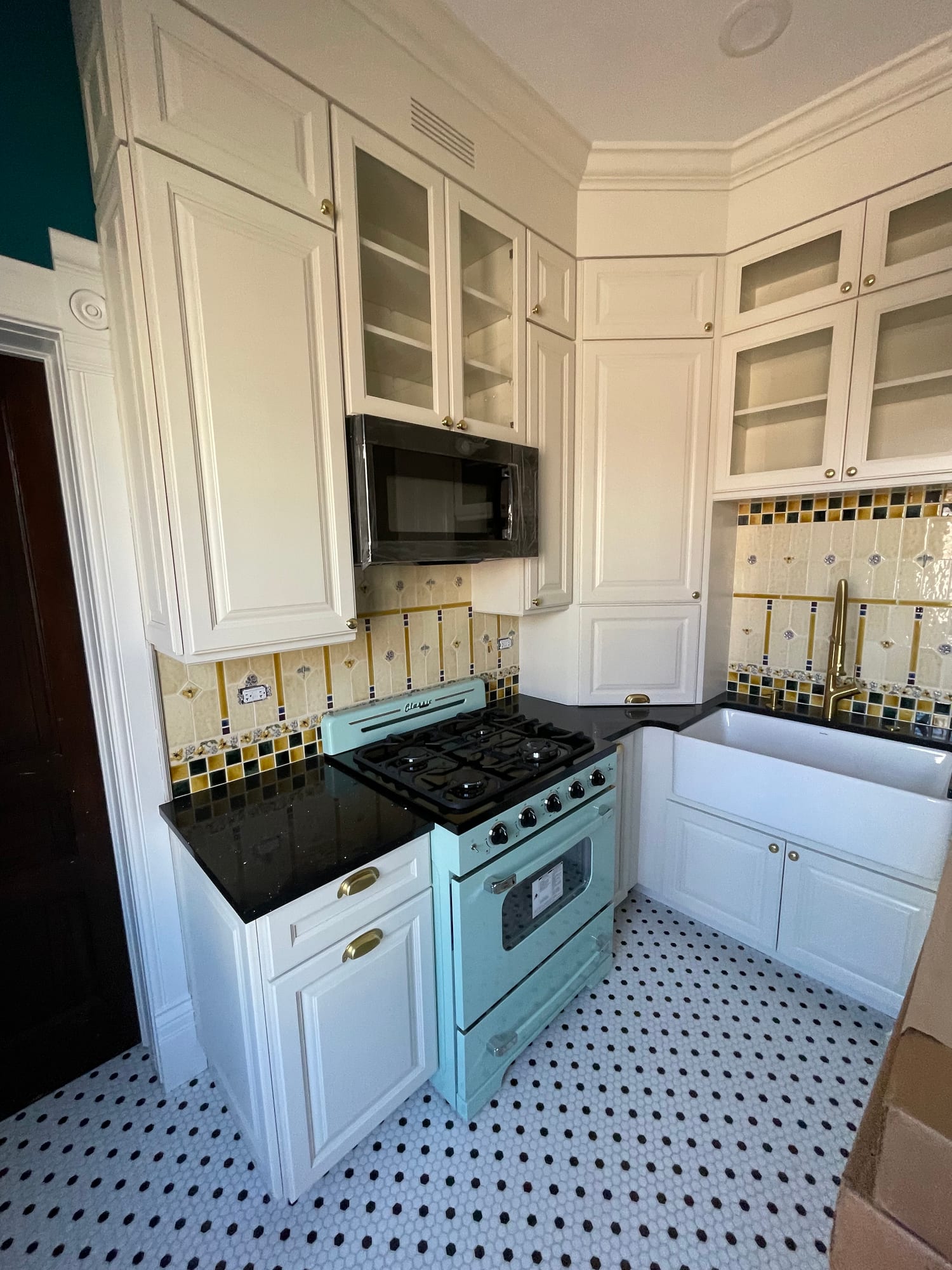Vintage style kitchen with cream raised panel cabinets, a mint range, patterned tile, a farmhouse sink and hex floor tile