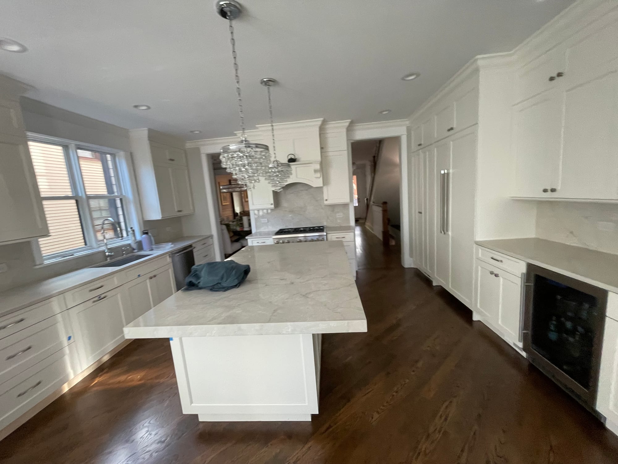 White Shaker kitchen with a thick-edged veined island, crystal pendants, a paneled refrigerator and dark wood floors