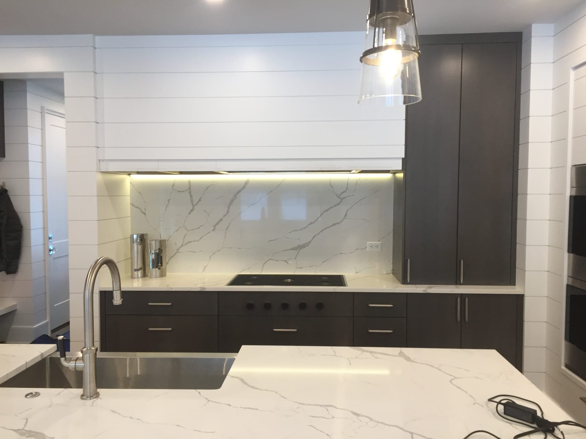 Cocina con muros y campana de tablones blancos, salpicadero veteado de altura completa y gabinetes oscuros lisos
