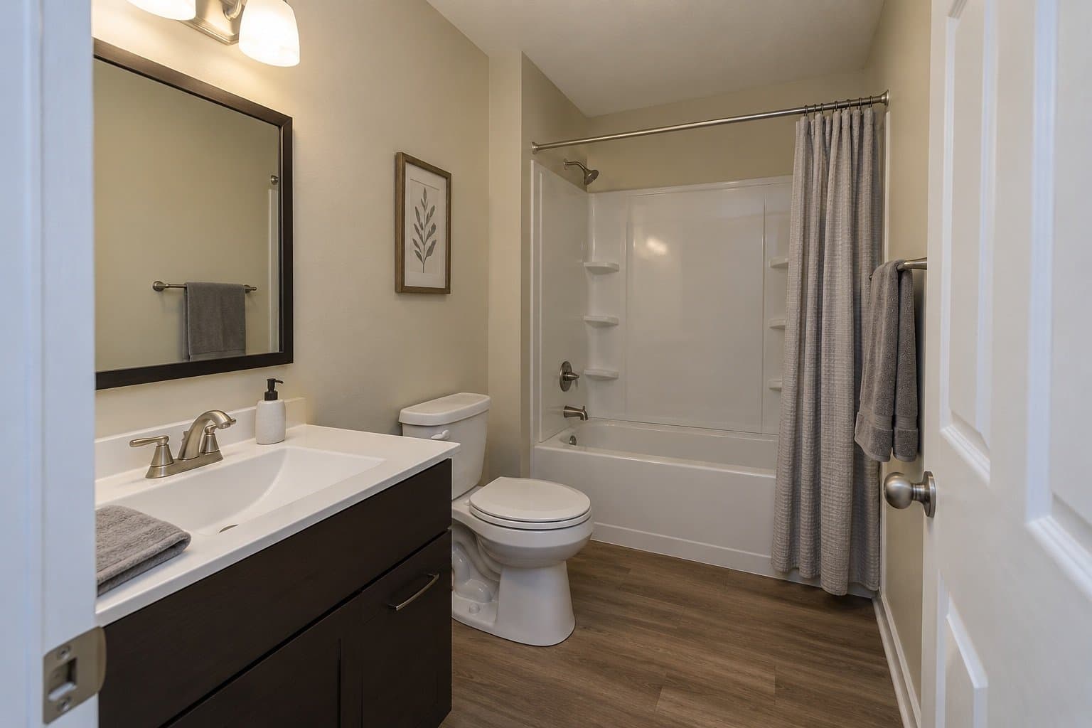 Simple bathroom with a dark espresso vanity, a five-foot tub with a one-piece acrylic surround, a grey curtain and wood-look flooring