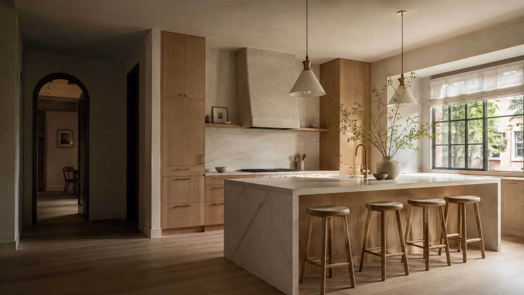 Wide kitchen with white oak cabinetry, a plaster range hood, a waterfall marble island with four oak stools and a large steel window