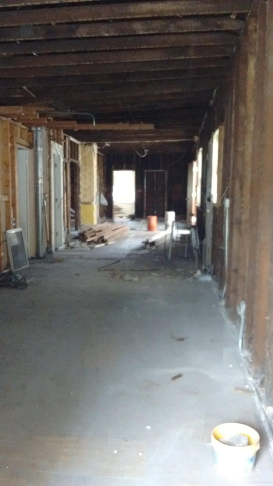 Long room gutted to the joists and studs, with the old plaster and ceiling removed, a stack pipe exposed and new lumber stacked on the floor