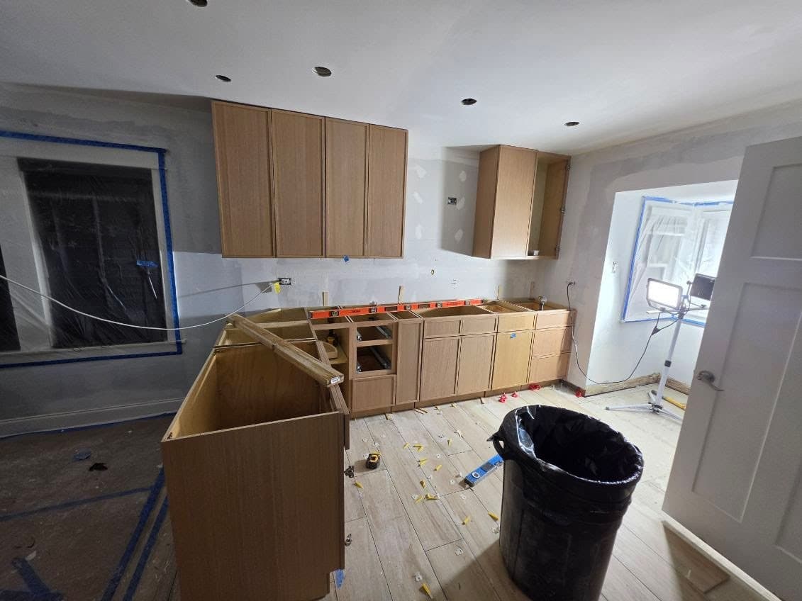 Rift oak upper and base cabinets set level along the wall, with the island cabinets and a temporary brace in place before the countertop template