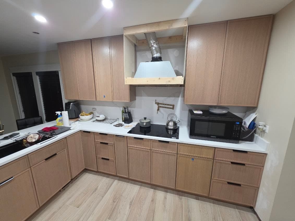The same kitchen finished, with rift oak cabinets, a white quartz counter and backsplash, a black hood and light wood-look tile floors