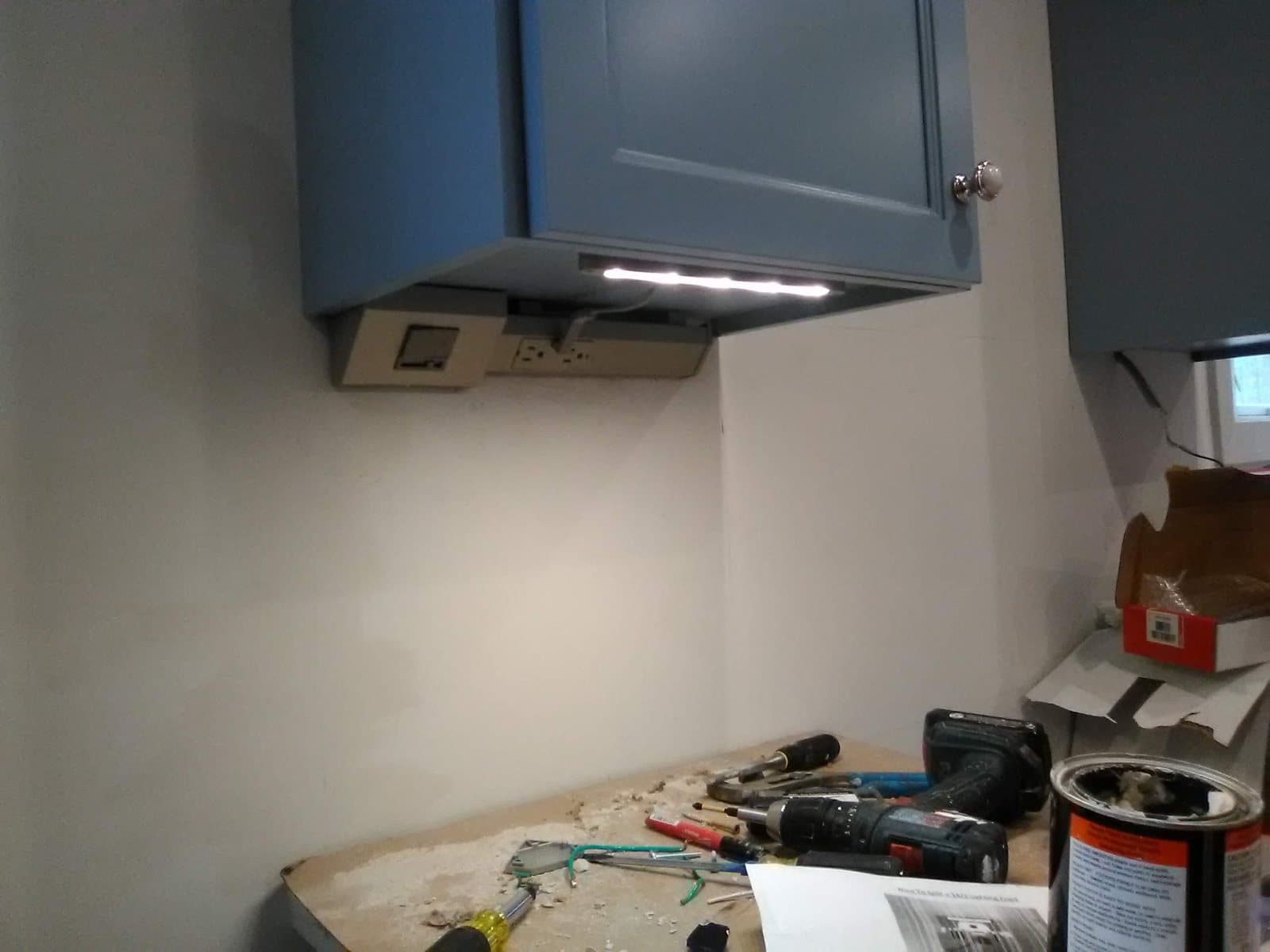 Under-cabinet LED strip lit beneath a blue cabinet, with the outlet strip and its controller mounted under the cabinet during trim-out