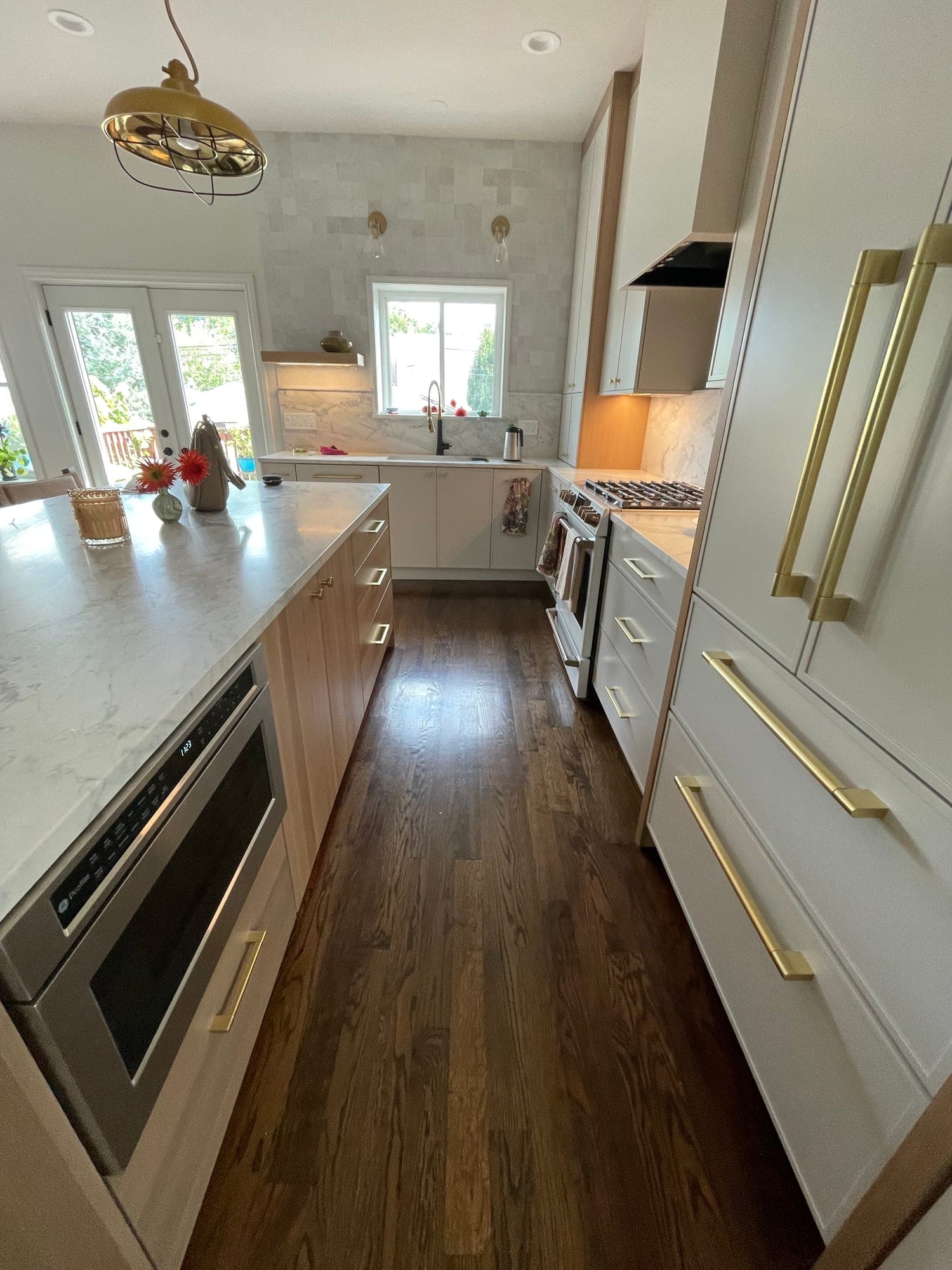 Kitchen with putty cabinets and long brass pulls, a wood island with a light veined top and dark wood floors