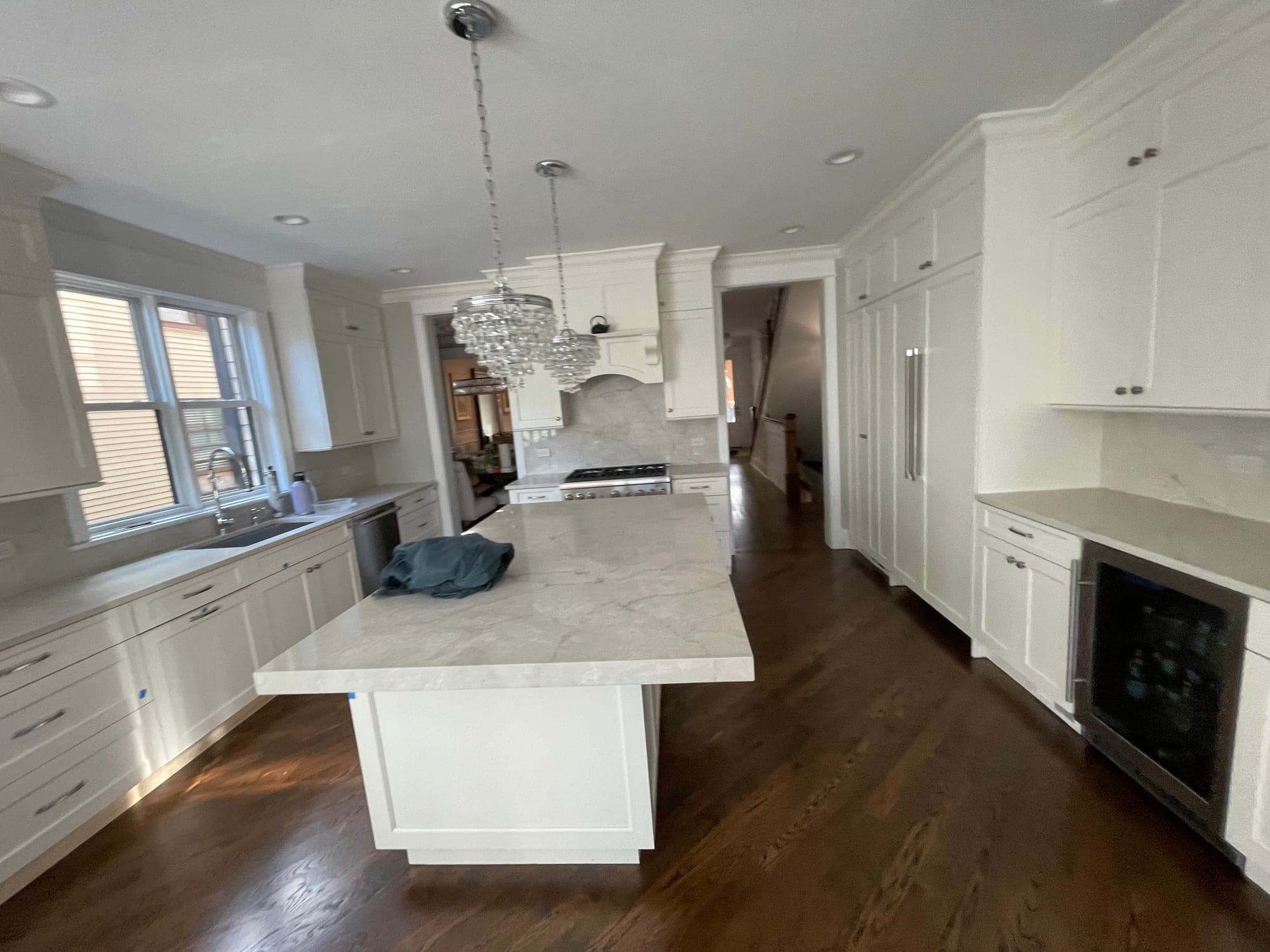 White Shaker kitchen with a thick-edged veined island, crystal pendants, a paneled refrigerator and dark wood floors