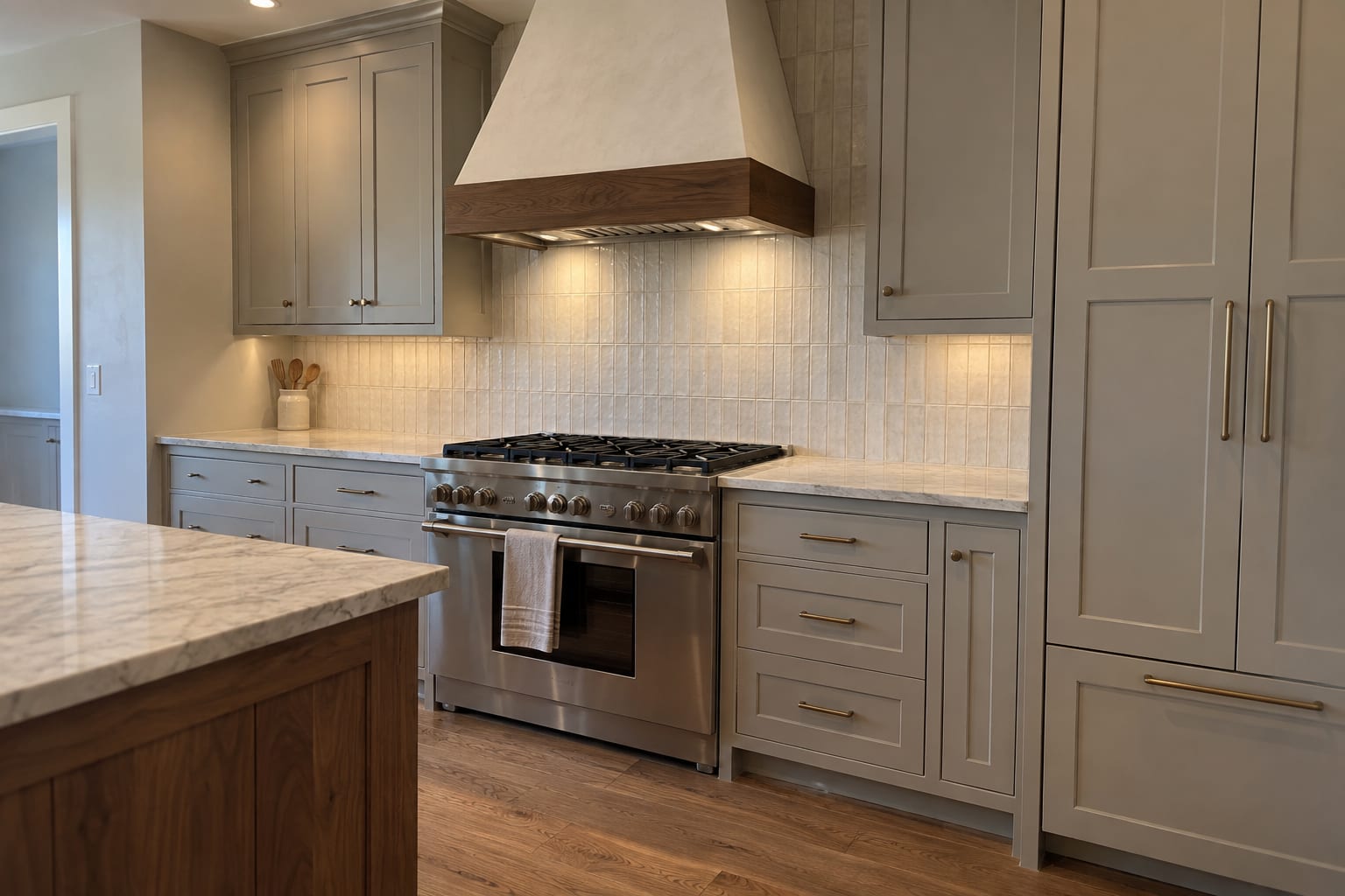 Range wall with warm gray inset cabinetry, a plaster hood trimmed in walnut, a wide stainless range and the corner of a walnut island with quartzite counters